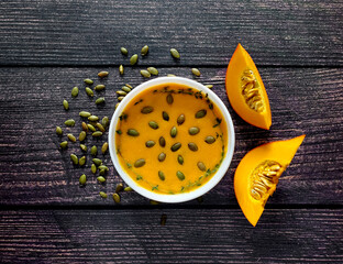 Pumpkin cream soup with pumpkin seeds and thyme, pumpkin slices on wooden background, top view 