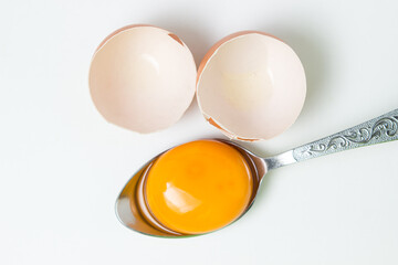 Egg yolk in a spoon next to the shell on a white background. Broken chicken egg.