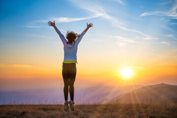 Young woman jumping at sunset mountains