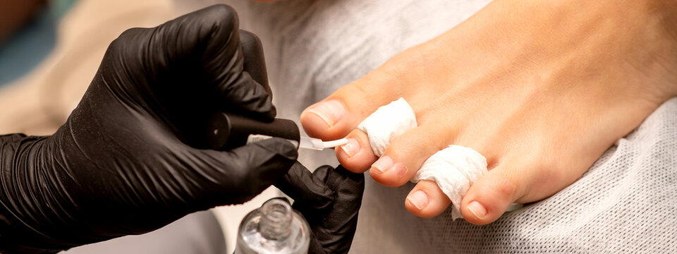 Manicure Master Painting Nails On A Female Foot With Transparent Nail Polish In A Beauty Salon, Close Up