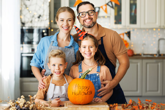 Happy family mother, father and children smiling  at camera with pumpkin during   celebration, preparing home Halloween decorations