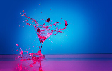 Martini cocktail splash over blue background in pink neon light. Nightlife, party