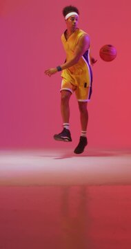 Vertical video of biracial male basketball player throwing ball on pink background