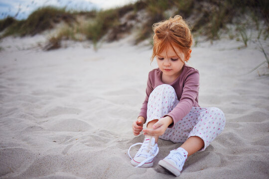 cute redhead baby girl having fun at the beach, playing with sand at autumn day