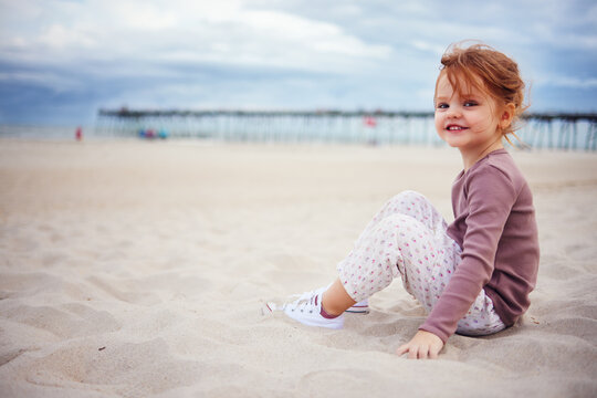 cute redhead baby girl having fun at the beach, playing with sand at cloudy day