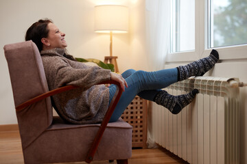 Woman heating feet on a chilly winter day, enjoying inside, energy and gas crisis, cold room,...