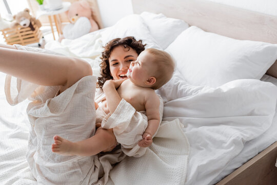top view of happy woman in loungewear lying on bed with cheerful baby daughter.