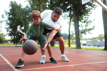 Obraz premium Father and son at public basketball court playing basketball.