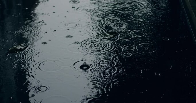 Close-up of drizzling torrential rain hitting a puddle during a suburban storm. Raindrops splashing on reflecting water surface. Monsoon season. Downpour. Rainfall