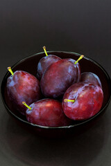 Fresh plum. Autumn harvest. Ripe purple plums in glass bowl on dark background. Concept: seasonal fruits, healthy food. Top view. Close up. Vertical. Copy space