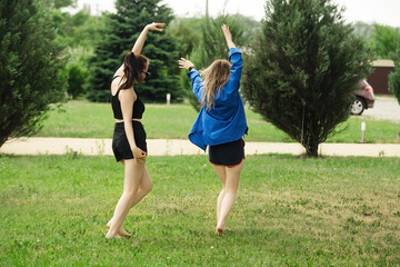 Obraz premium two beautiful girls girlfriends have fun and dance in the summer on vacation, dressed in swimwear and sportswear on a bright green meadow