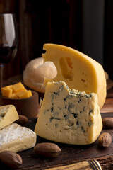 Varied cheese table, blue cheese Fontina Gruyer Cheese Teetilla in wooden table with red wine glass Pimentero oil and Round homemade fields of field and rustic knife
