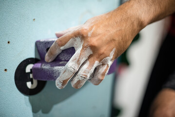 Hand holding on to a climbing hold on a climbing wall.