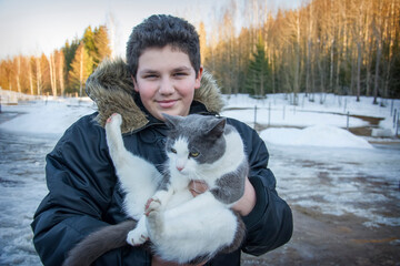 In the spring, a boy holds a big cat in his arms on the street.