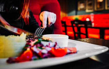 woman hands with fork and knife eating food in cafe