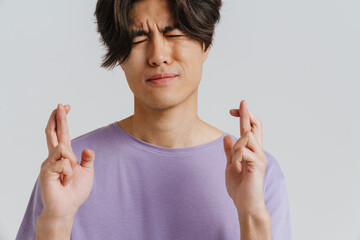 Young asian man grimacing while making gesture for best luck