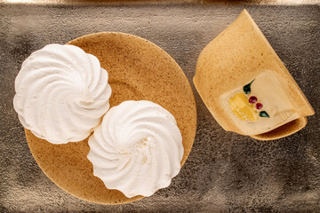 Two sweet white marshmallows on a ceramic saucer with a cup on a metal tray, macro, top view.