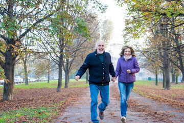 Senior adult married couple outdoors running free having fun holding hands