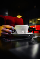 woman hands holding a white cup of tea or coffee standing on the table in cafe
