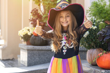 Cheerful little girl in a witch costume near the house on the day of the Halloween holiday and...