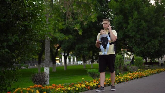 A young man walks in the park with a newborn child