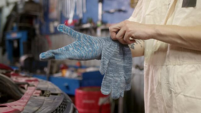 In car service, unrecognizable woman worker puts gray gloves on her hands and prepares for regular car maintenance work. Close up view of girl putting on gloves at work.