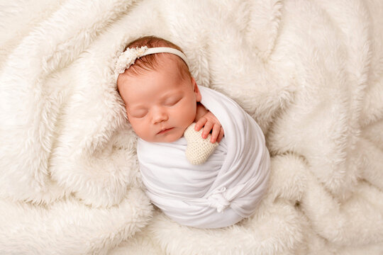 Top view of a newborn baby girl sleeping in a white cocoon with a white bandage and a flower on her head on a white background. Beautiful portrait of a little girl 7 days, one week. Macro photography.