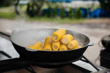 Yellow cobs of corn are grilled in a large black pan. Street food and smoke