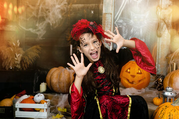 Portrait of child in wearing black witch costume, makeup, screaming, scares in carnival night surround by web, carved pumpkins. Girl having fun, trick or treat. Halloween holiday concept