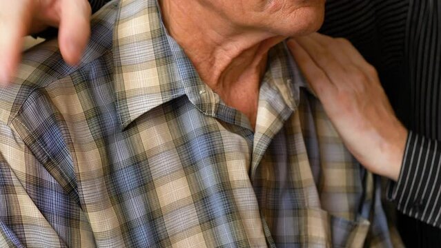 close-up a man claps his shoulders and hugs a Caucasian pensioner 70-80 years old sitting at home. caring for the elderly, friendship in the family, the son visited his elderly father,