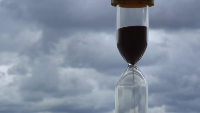 Timelapse hourglass on blue clouds background. Time is running out. The sand in the clock is pouring and fluffy clouds are floating.