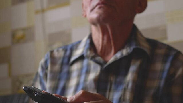 an elderly man carefully watches tv holding a remote control while at home. selective focus. a pensioner watches tv. home leisure. real people. TV programs for the elderly