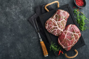 Steaks Raw. Raw cowboy steak, marbled beef meat with spices rosemary and pepper on black wooden...