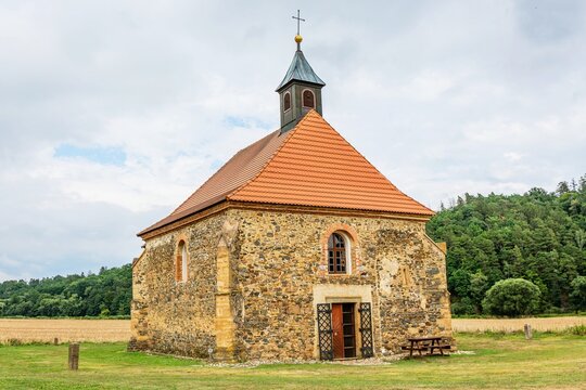 Dolany, Czech Republic - July 30 2022: View of gothic church from 13th century made of stone dedicated to Saint Peter and Paul, standing in the middle of fields. Green forest in the background.