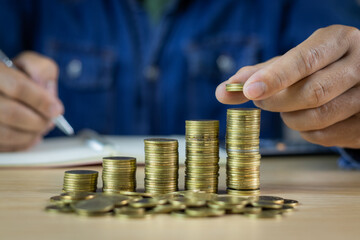 Man holding coins on wooden table and writing in notebook, income and expenses accounting concept, saving for retirement, saving money for inflation during economic downturn, financial planning