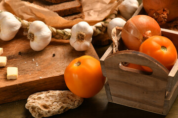 still life of food in a rural style on a dark wood background, onion and tomatoes in a box, galic, concept of healthy food