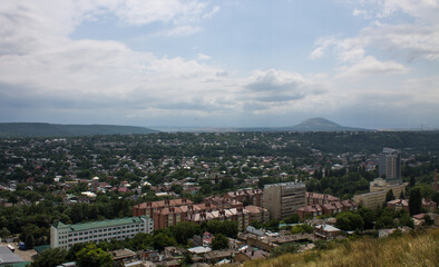 Fototapeta na wymiar Panoramic top view of Pyatigorsk, Stavropol territory with residential buildings among green trees and cloudy sky above the horizon