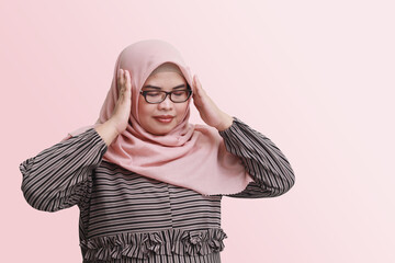 Portrait of sick Asian woman with hijab, having a migraine, touching his temple. Isolated image on pink background. Headache disease concept