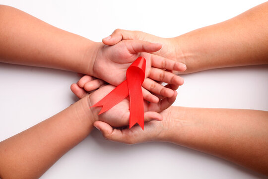Close up photo of woman's hand and child's hand holding red ribbon together. Aids day concept