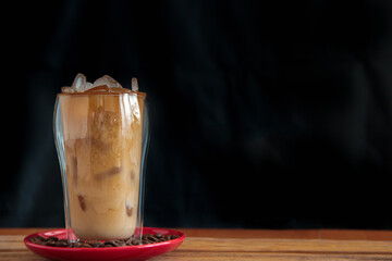 Ice coffee in a tall glass and pouring milk from above with coffee beans on the table in red plate.