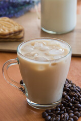 Ice coffee in a tall glass and pouring milk from above with coffee beans on the table in red plate.