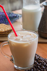 Ice coffee in a tall glass and pouring milk from above with coffee beans on the table in red plate.