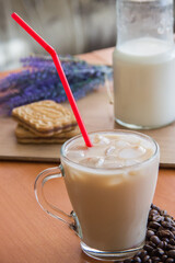 Ice coffee in a tall glass and pouring milk from above with coffee beans on the table in red plate.