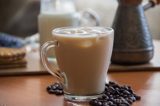 Ice Coffee In A Tall Glass And Pouring Milk From Above With Coffee Beans On The Table In Red Plate.