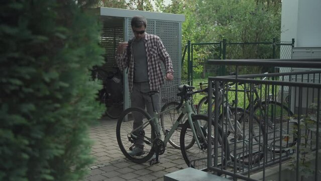Cyclist parks and locks his bicycle in bike parking lot outside home in Germany. Man fastening bicycle lock on parking in courtyard. Male arrived at home and parked cycle and secured it with lock