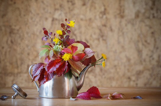 autumn bouquet in iron teapot on wooden table