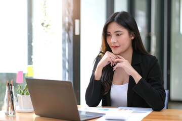 Beautiful Asian business woman sitting working on laptop in office.
