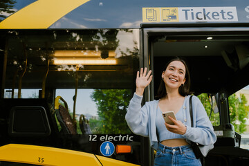 Young beautiful smiling asian girl with phone waving