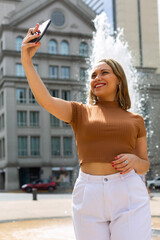 Woman taking selfie with smartphone on background of beautiful fountain in Southamerica. Traveling on a summer day concept. Female traveler visiting landmarks