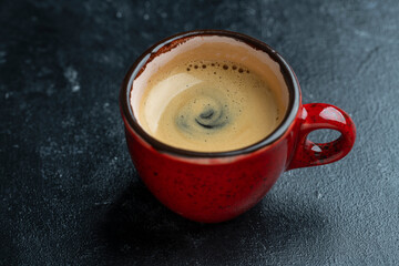 Fresh aromatic morning coffee in red cup on a black background, closeup